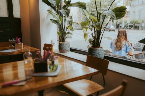 Blick aus dem Capra nach draußen. Man sieht einen eingedeckten Eichenholztisch mit einer Blumenvase und Pflanzen auf der Fensterbank