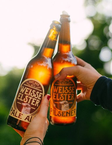 Anstoßen mit zwei Flaschen Weisse Elster Bier (Pilsener und Pale Ale) in der Abendsonne